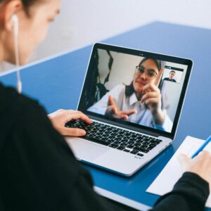 Woman participating in a virtual meeting, taking notes during a video conference on a laptop.